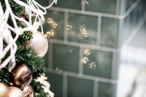 A close-up view of a decorated Christmas tree against a minimal tiled wall